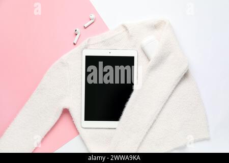 Elegante maglione femminile, tablet computer e auricolari su sfondo colorato Foto Stock