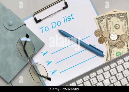 Composizione con lista delle cose da fare, portafoglio, denaro e occhiali da vista su sfondo grigio. Concetto di gestione del tempo. Primo piano Foto Stock