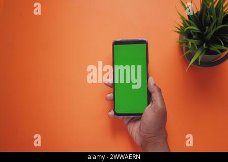 vista dall'alto della mano di un giovane uomo che utilizza uno smartphone con schermo verde su sfondo arancione Foto Stock