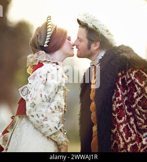 Medievale, re e coppia si baciano nella storia con la moda rinascimentale all'aperto con matrimonio e amore. Vintage, giardino e leader reale con regina Foto Stock