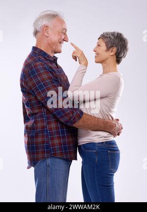 Senior, coppia e felice abbraccio in studio insieme, sorridere e pensionati in relazione d'amore con anziani. Indicante, persona femminile con uomo in bianco Foto Stock