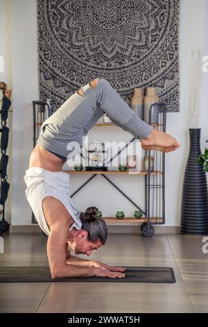 Vista laterale del giovane maschio flessibile che fa Vrischikasana durante l'allenamento di fitness a casa Foto Stock