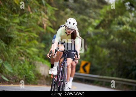 giovani atleti di ciclismo asiatici che cavalcano in bicicletta all'aperto su strade rurali Foto Stock