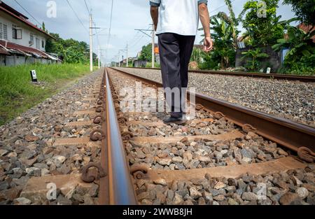 Un uomo che cammina sui binari ferroviari intorno agli insediamenti nelle aree rurali dell'Indonesia. Foto Stock