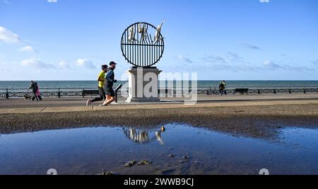 Brighton Regno Unito 23 marzo 2024 - i corridori passano accanto alla scultura Flight of the Langoustine su Hove Plinth sul lungomare in una mattinata soleggiata ma fredda lungo la costa meridionale. La scultura è stata creata dallo scultore di Brighton Pierre Diamantopoulo ed è la seconda ad abbellire Hove Plinth : accreditamento Simon Dack / Alamy Live News Foto Stock