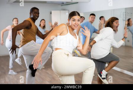 Eccitati uomini e donne multietnici che esercitano movimenti attivi con ginocchio sollevabile in un centro di danza al chiuso Foto Stock