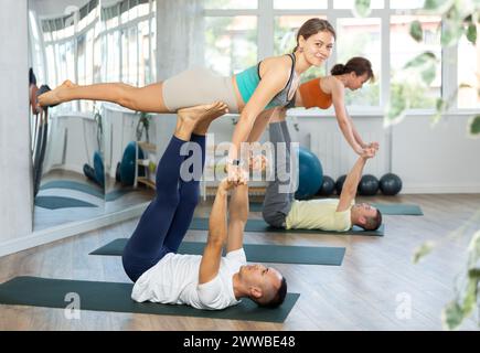 Gli amanti dello stile di vita attivo eseguono un asana da guerriero volante yoga in coppia in palestra Foto Stock