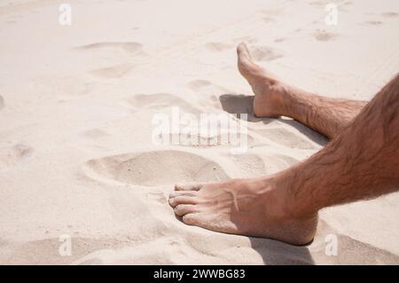I piedi dell'uomo giacciono sulla sabbia. Vista ravvicinata. Foto Stock