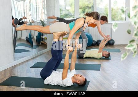 Gli amanti dello stile di vita attivo eseguono un asana da guerriero volante yoga in coppia in palestra Foto Stock