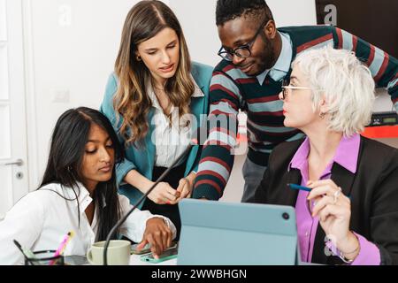 Un gruppo diversificato di professionisti impegnati in una discussione collaborativa con i dispositivi digitali - interazione e tecnologia - ambiente di ufficio multiculturale Foto Stock