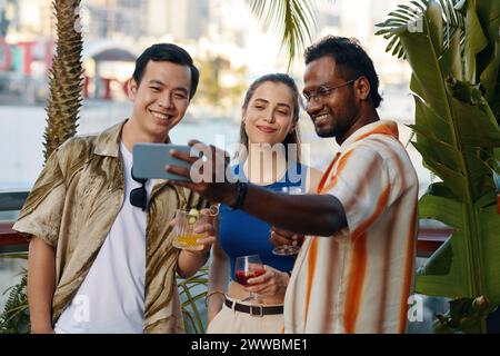 Felice uomo indiano che fa selfie con gli amici alla festa al bar Foto Stock