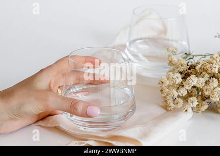 Persona che prende un bicchiere d'acqua. Tazza di vetro contenente acqua naturale su sfondo bianco. Immagine semplice e pulita. Concetto di semplicità dell'acqua potabile. Foto Stock