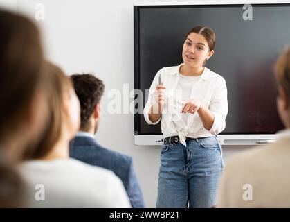 Una coach femminile qualificata e positiva che spiega l'argomento a un gruppo di persone durante una lezione di lingua straniera nell'auditorio Foto Stock