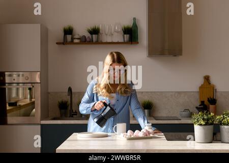 Donna che versa caffè in una cucina moderna. Ora del caffè, routine mattutina Foto Stock