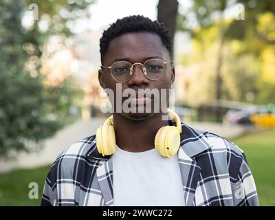 Ritratto di un giovane studente afroamericano con occhiali e cuffie che guardano seriamente la fotocamera Foto Stock