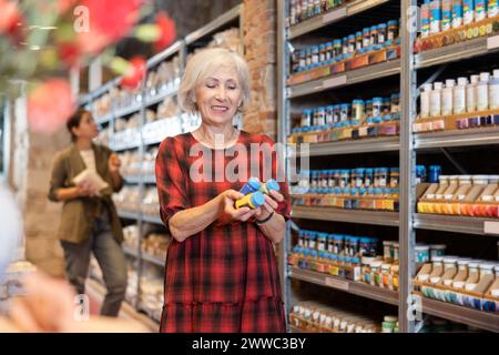 La donna anziana sceglie pigmenti multicolore per i suoi futuri piatti in argilla o ceramica in un negozio specializzato Foto Stock