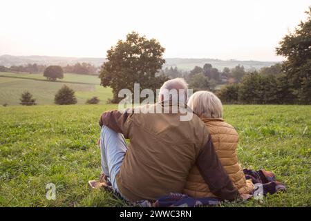 Vista sul retro della coppia senior seduta su un prato godendosi il tramonto Foto Stock