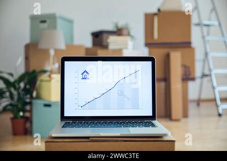 Linea di salita il grafico su schermo di computer portatile nella parte anteriore delle scatole di cartone in una stanza vuota in una nuova casa Foto Stock