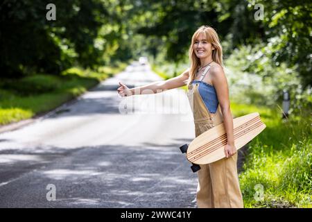 Una donna felice che va in giro e tiene in mano lo skateboard nella foresta Foto Stock