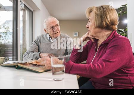 Uomo e donna senior seduti con album fotografico a tavola Foto Stock