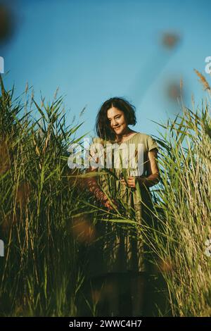 Donna matura in piedi in mezzo a canne alte sul campo nelle giornate di sole Foto Stock