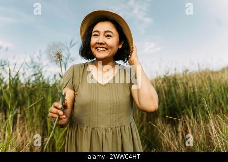 Donna matura felice che tiene il dente di leone sul campo Foto Stock