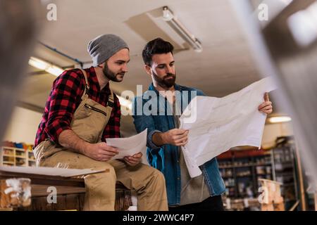 Giovani falegnami che leggono il progetto in officina Foto Stock