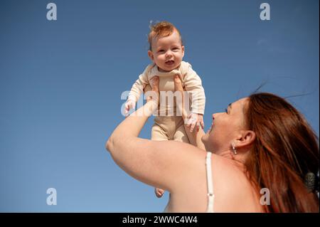 Donna felice che tiene una figlia sotto il cielo blu Foto Stock