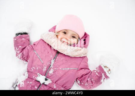 Ragazza giocosa che indossa una giacca invernale e sdraiata sulla neve Foto Stock