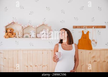 Donna felice incinta in piedi davanti al muro a casa Foto Stock