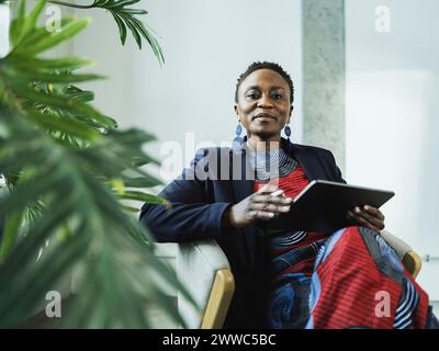 Elegante donna d'affari con un PC tablet seduto su una sedia in ufficio Foto Stock