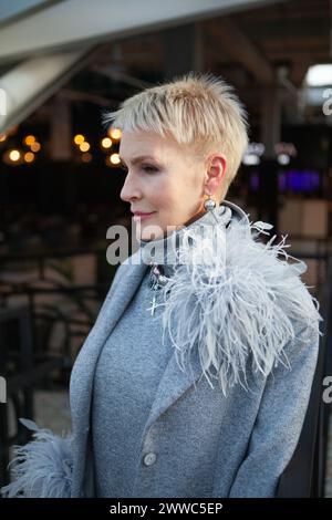 Ritratto di una donna matura con un taglio di capelli corto, vestito con una tuta grigia piuma e accessori alla moda, che mostra una tendenza alla moda Foto Stock