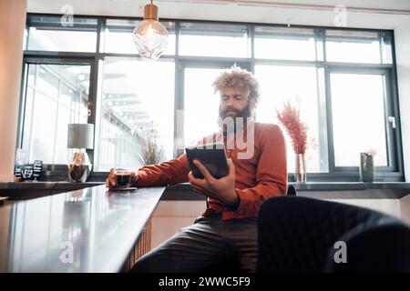 Uomo d'affari maturo seduto e che utilizza un tablet PC nella caffetteria dell'ufficio Foto Stock