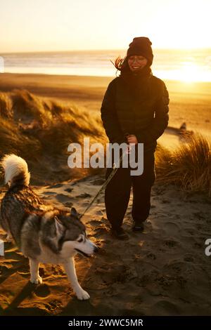 Giovane donna felice che cammina cane Husky in spiaggia Foto Stock