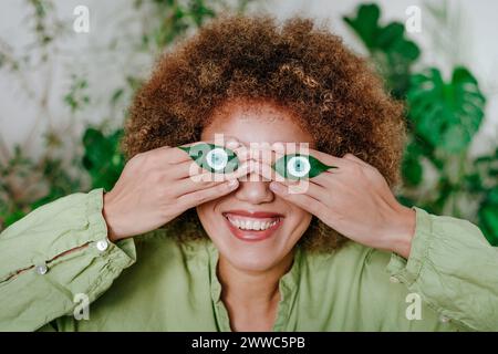 Giovane donna felice con gli occhi dipinti sulle foglie a casa Foto Stock