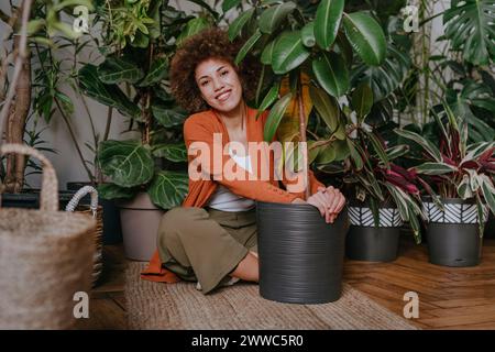 Sorridente giovane donna seduta con piante su tappeto Foto Stock