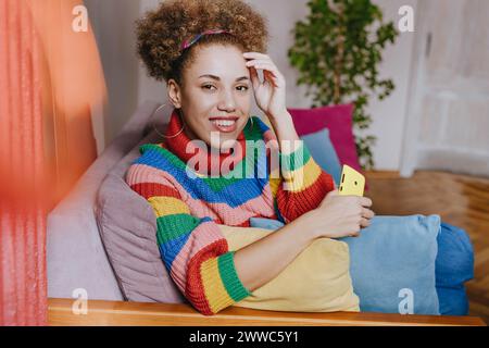 Giovane donna felice seduta con uno smartphone sul divano Foto Stock