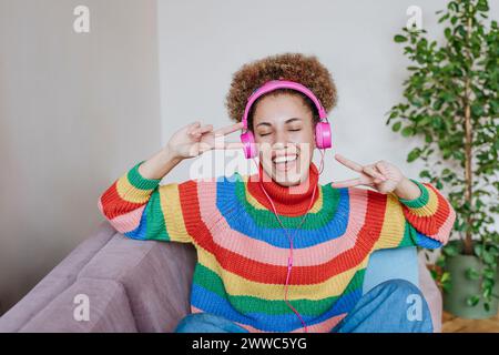 Donna felice che ascolta la musica e mostra un gesto di pace Foto Stock