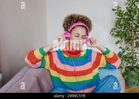 Giovane donna felice che ascolta la musica attraverso le cuffie a casa Foto Stock