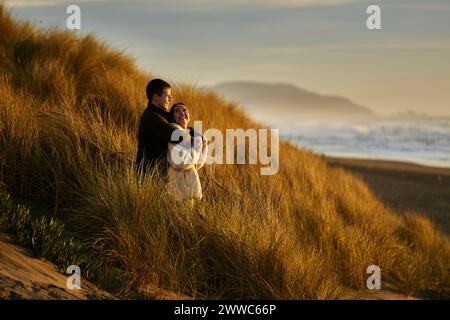 Coppia sorridente che abbraccia e si trova sulla spiaggia dell'oceano Foto Stock