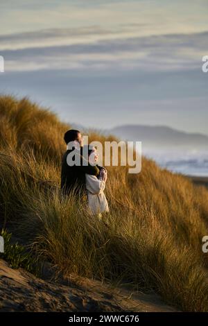 Uomo che abbraccia la ragazza da dietro in piedi in una duna in spiaggia Foto Stock