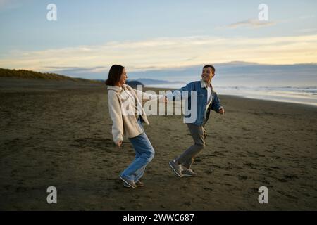 Uomo sorridente che tiene per mano la fidanzata e cammina sulla spiaggia Foto Stock