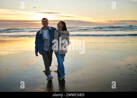 Uomo sorridente che cammina con la fidanzata sulla spiaggia dell'oceano Foto Stock