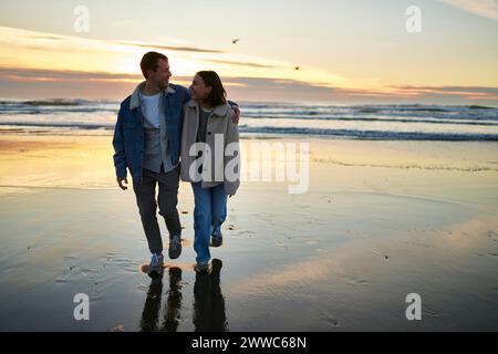 Uomo e donna sorridenti che camminano insieme sulla spiaggia dell'oceano Foto Stock