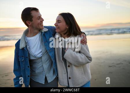 Uomo sorridente con un braccio intorno alla ragazza che cammina in spiaggia Foto Stock