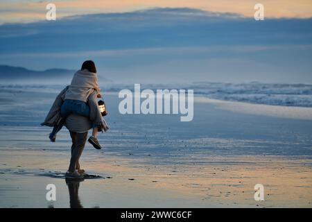 Fidanzato che porta con sé la fidanzata e cammina sulla spiaggia al tramonto Foto Stock