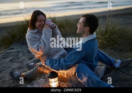 Giovane donna sorridente che fotografa un uomo con la macchina fotografica in spiaggia Foto Stock