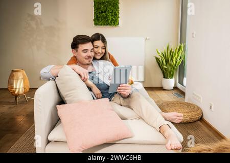 Sorridente giovane coppia che usa un tablet PC sul divano Foto Stock