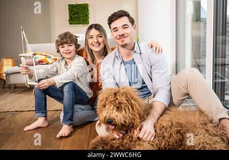 Famiglia felice con casa modello e cane seduto nel soggiorno Foto Stock