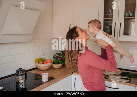 Madre sorridente che abbraccia e gioca con la bambina in cucina Foto Stock